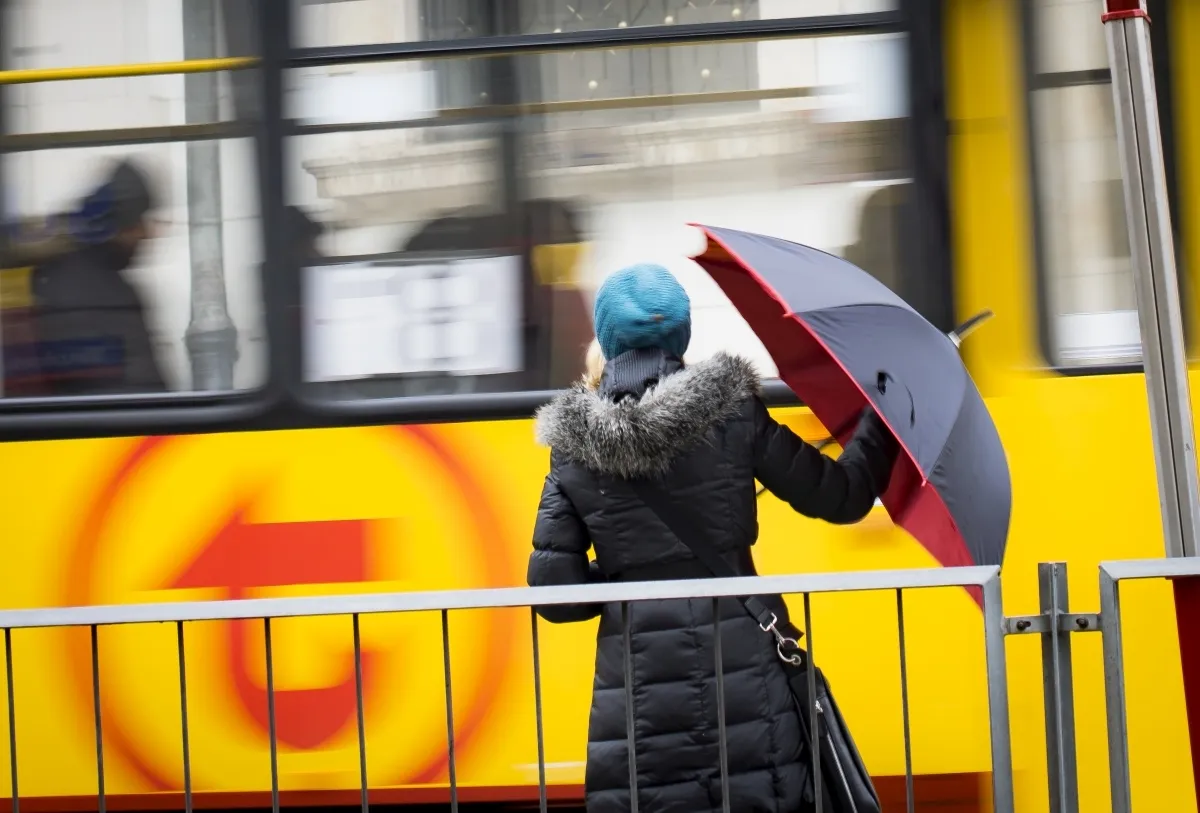 Person carrying a red-and-white umbrella beside a blurred yellow tram